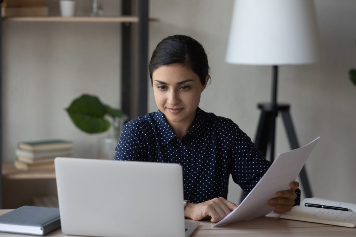 Young Indian businesswoman work on laptop with paperwork