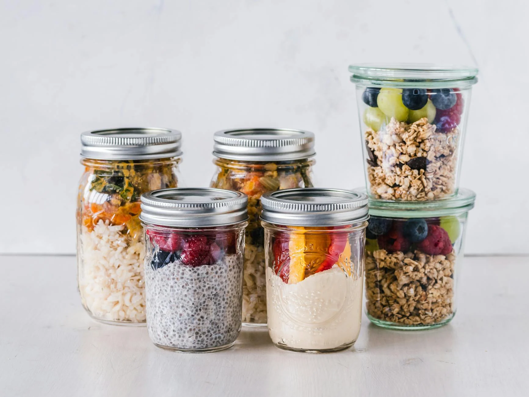 overnight oats - six fruit cereals in clear glass mason jars on white surface